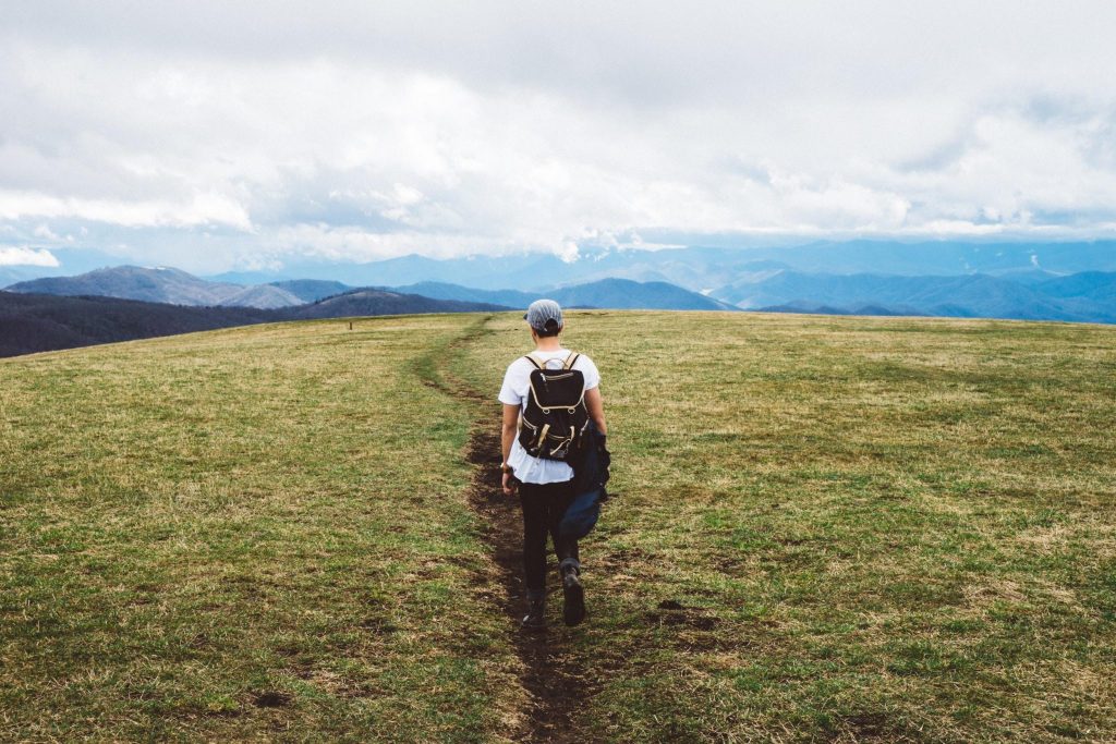person-walking-trail-open-field-mountains